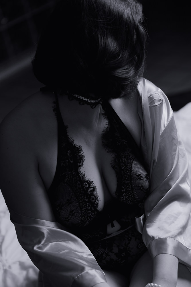 A moody black and white image of a boudoir pose with a mysterious woman as the subjec.t