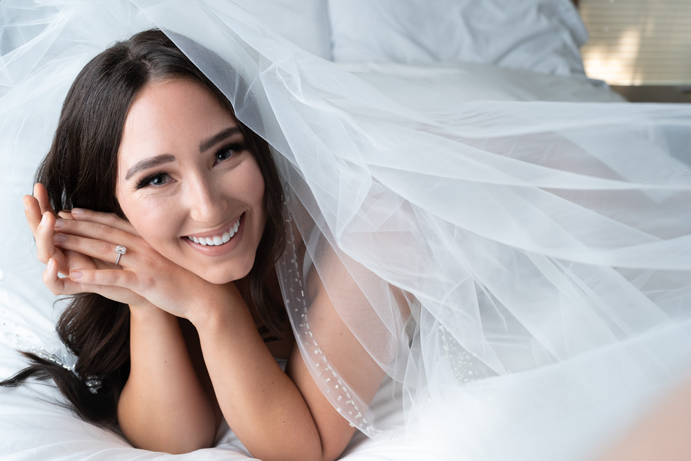 A young woman swimming her wedding veil in a boudoir pose. She is smiling and her ring is glowing.